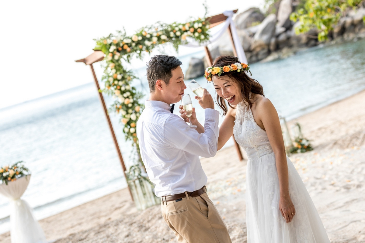 Eri and Wonseok toasting their wedding day on the beach at Koh Tao at the elopement wedding planned by Forever Lovestruck.